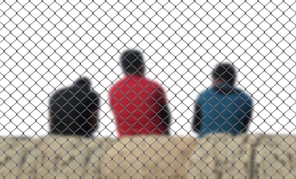 three men sitting on the other side of wired fence
