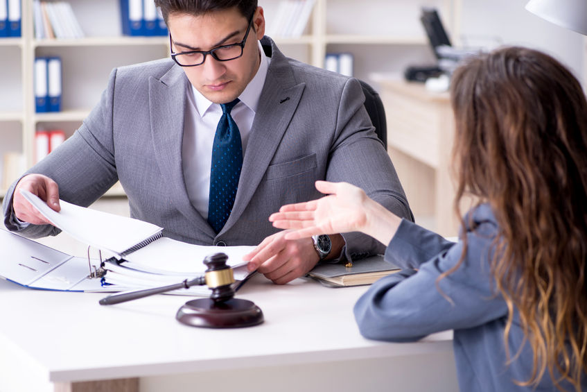 Man in a gray suit reviewing documents with a woman across a desk, with a gavel on the table.