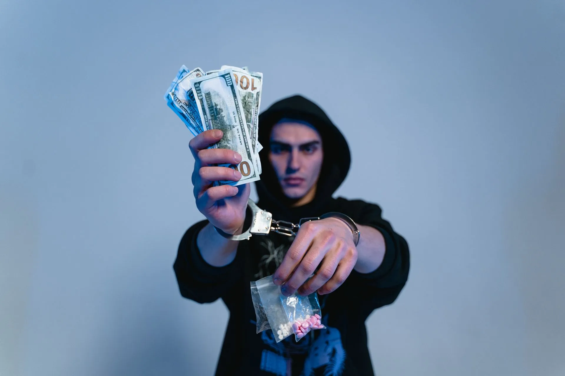 Person in handcuffs holding cash and a bag of pills, illustrating drug possession and distribution charges in Arizona.